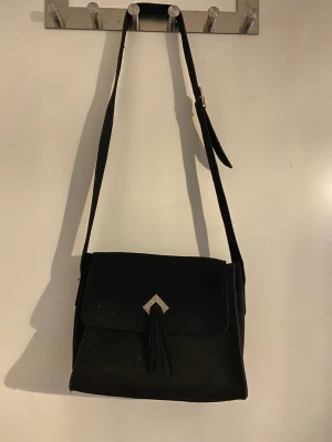 Axelremsväska i äkta mocka - Axelremsväska i jättebra kvalitet i äkta mocka. Perfekt storlek att ha till vardags som crossbody. Söta detaljer på framsidan och axelrem som gör att justera