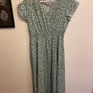 Sommarklänning - Grön sommarklänning med vita blommor och resårmidja! Storlek M. Oanvänd! Finns på fler sidor också 🥰