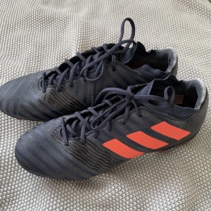 Fotbollsskor adidas nemeziz - Fotbollsskor i väldigt bra skick. Marinblå/grå med neonrosa detaljer. Användts fåtal gånger och helt nytvättade - lätta att tvätta i maskin. Storlek 40 Väldigt mjuk häl. Benskydd finns i annat inlägg