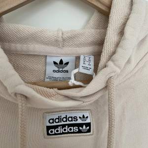 Cropped hoodie från Adidas, strl 34. Använd en gång sen tvättad. Beige. Något ljusare i verkligheten än på bild. Första inzoomade bilden visar mest korrekt färg.