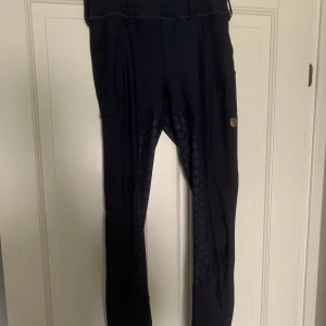 Maya Delorez performance - Ett par helskodda marinblå Maya Delorez performance ridbyxor i storlek M. I stort sätt nyskick, dock ett litet hål i fickan. Hålet kommer från en nafsande häst, men är knappt märkbart.