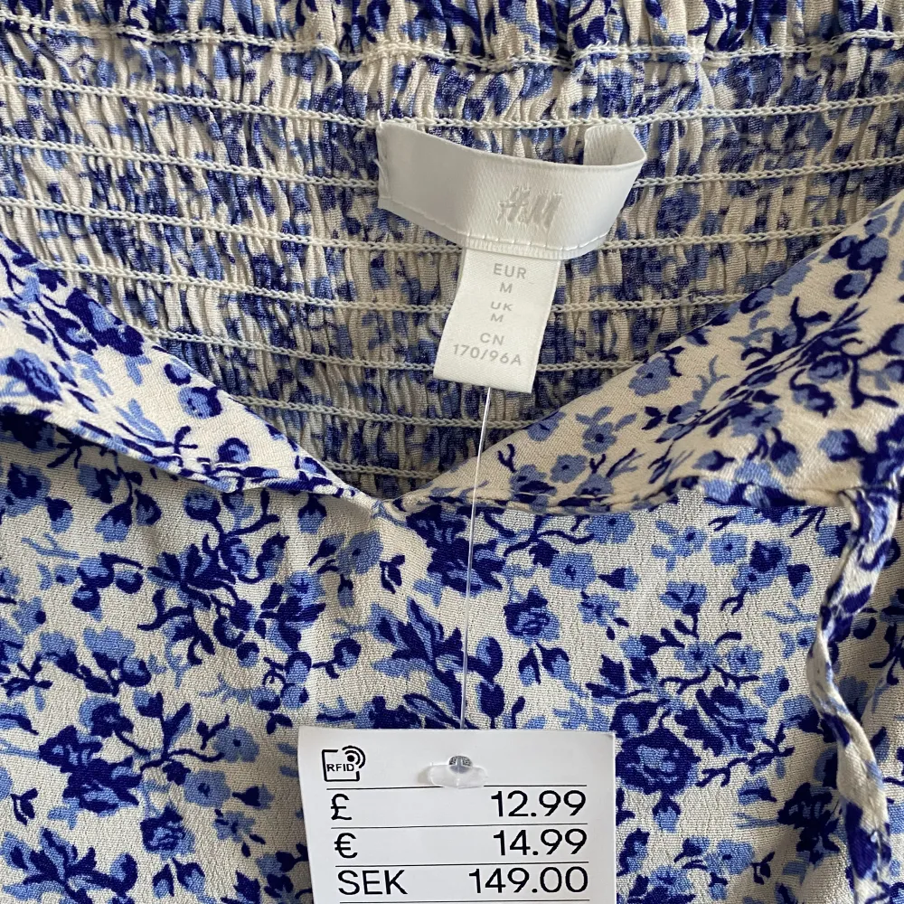 Somrig vit topp med blå blommigt mönster från H&M. Helt oanvänd i nyskick, lappen sitter kvar. Köpt för 149kr säljer för 40kr.. Toppar.
