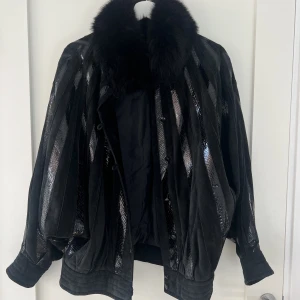 Mockajacka med pälskrage - Så sjukt cool jacka i bomberstil med pälskrage. Lite mer unik version av Meotine. Jackan är i mocka och har ränder med ormskinn. Färgen är svart. Storlek L, snyggt oversized. Köpt second hand och knappt använd. Har en lös knappt men den går att sy på. 🤍🤍🤍