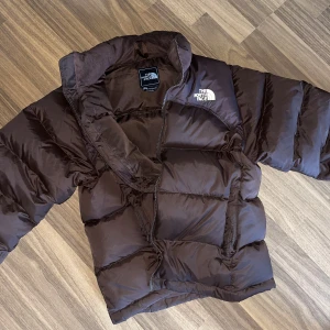 Brun TNF Nuptse (sällsynt) - Nu är det dax att sälja min jacka. Har använts ett 10 tal gånger endast då den sitter lite tajt på mig som kille. Det är storlek M unisex så därför sitter den som S. Går att spänna åt vid midjan. Köptes på grailed för 4000kr!
