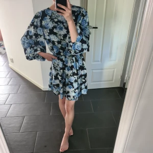 Blommig klänning - En blå svart blommig klänning från "In the style" i UK 8. Passar som 34/36. Klänningen har ballongärm och är perfekt till sommaren. Endast använd en gång och köptes för ca 500kr. Pris kan diskuteras. Köparen står för frakten och fraktar endast på helger.