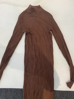 Brun klänning  - Brun klänning som slutar vid knäna, har en liten krage vid halsen och är långärmad. Tog bort lapparna och använde en gång ca 1h men insåg att det inte var min stil då jag inte gillar krage