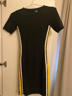 Svart klänning - Svart klänning med gula, vita detaljer. Använd några få gånger, bra skick