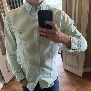 Grön Ralph Lauren Skjorta - En perfekt skjorta när man vill lyxa till vardagen eller helgerna. Modellen i bilden är 177Cm. Skicket på skjortan är 9/10, och har inga defekter. Skjortan är Slim Fit i storlek S. Original priset är 1349kr men säljer för 449