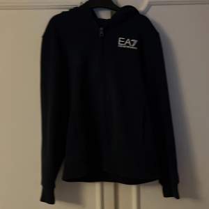 En snygg och fräsch zip hoodie skick (10/10)  använd 2 gånger  tröjan är från EA7 (Emporio Armani) size 150 cm. Hör av er om ni har frågor!!