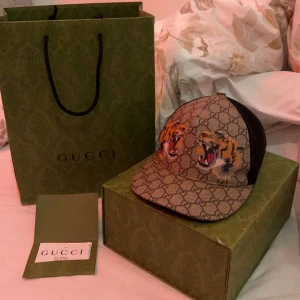 Gucci tiger vintage keps  - 2000 minsta priset kom med bud… Märke: GUCCI Färg: Beige / Svart / Gul Material: PVC-läder / GG Canvas Storlek (cm): Storlek (tum): Stil: Keps Vi skickar endast föremålet som visas på bilden. Skick: Utmärkt.  Äkta 