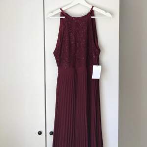 Röd långklänning med plisserad kjol och öppning i ryggen med tre sidenband.  Oanvänd, köpt på bubbleroom! 🌻