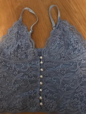 Bik bok topp M - Passar A, B och C kupor, annars lite liten. Resår i ryggen så passar nog S och L också. Justerbara band. Riktiga knappar där fram. Lite ljusare blå färg, spets.  Oanvänd