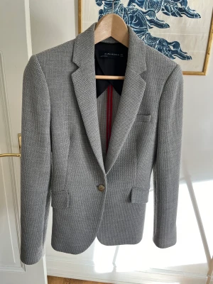 Blazer / kavaj Zara Woman - Snygg blazer från Zara. Ljusgrå, tyg med struktur. En guldknapp. Bra skick. Ganska liten i modellen, passar också XS