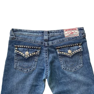 True Religion Jeans - Trueys i modellen ”RAINBOW BILLY”. Midjemått 39,5cm. Innerbenet 77cm. Ytterbenet 100cm. En nit har gått av.