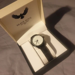 Klocka - Stilrent analogt armbandsur från Brave Soul. Armbandskedja i mörkgrå/svart färg och små strass stenar som siffermarkörer. Helt ny och oanvänd i originalförpackning! Tyvärr fel storlek för mig :(
