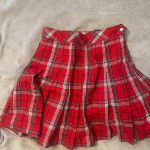 En rutig röd kjol i nyskick. Säljs för den har blivit för liten. Stolek 34 från Divided.