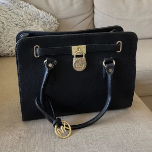 Väska  - Michael Kors Väska ( 27cm x 14cm). Svart läder med guldiga detaljer. Kan stå av sig själv och rymmer otroligt mycket. Perfekt för skola och vardag :)