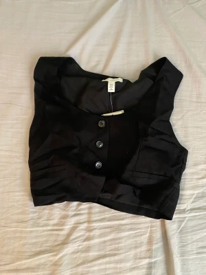 Väst hm  - Säljer en svart väst-topp från H&M i storlek xs. Aldrig använd, endast testad en gång. Prislapp kvar. Toppen är ganska stor i storleken (snarare storlek s). Nypris 149 kr