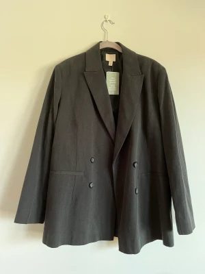 Oversized blazer i jeanstyg - Oanvänd over-sized blazer från H&M. Mörkgrått jeanstyg. Alla lappar kvar. Nypris 699kr