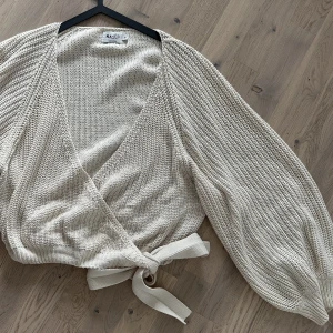 Stickad tröja  - Stickad cremevit omlotttröja med knyte i sidan. 