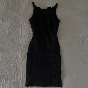 Svart klänning - Klänning med små rosor vid axelbanden. Materialet är texturerat och klänningens alla små detaljer gör den till den perfekta svarta klänningen för alla festligheter. Inga skavanker!