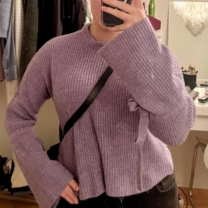 Stickad tröja  - Söt lila stickad tröja, ganska kort med fina långa armar som har rosetter på sig.