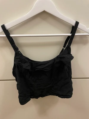 Svart croppat linne - Jättefint svart croppat ribbat linne ifrån hollister. Bra skick, knappt använt, och har även justerbara band! Fin voland längs överkanten. 