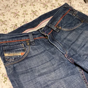 Mörkblåa dieseljeans  - Ett par supersnygga mörkblåa Diesel jeans, lågmidjade med flared legs och röda detaljer. Bra skick! ☺️midjemått: 76, innerbenslängd: 72, passar min vän som är 165 cm lång 💗