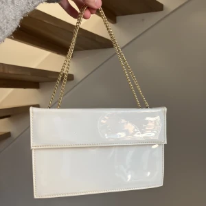 Vit handväska - Säljer den här gulliga vita handväskan med guld och som är blå inuti. Man kan ha den kort men om man vill ha den lite längre så den kan vara på axeln går det med! Säljer då den aldrig kommit till användning 💕