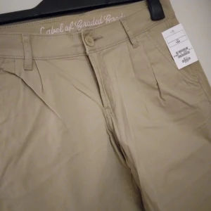NYA, oanvända beiga chinos / byxor. Storlek: 164 Cl. - Helt nya och oanvända beiga chinos-byxor från barn/ungdomsavdelningen, Storlek 164 Cl. Har fickor fram och bak + hällor för bälte/skärp, samt stängs med dragkedja och knapp. Material: Bomull. Etiketter sitter kvar sedan inköpet. Felfria. FRAKT TILLK