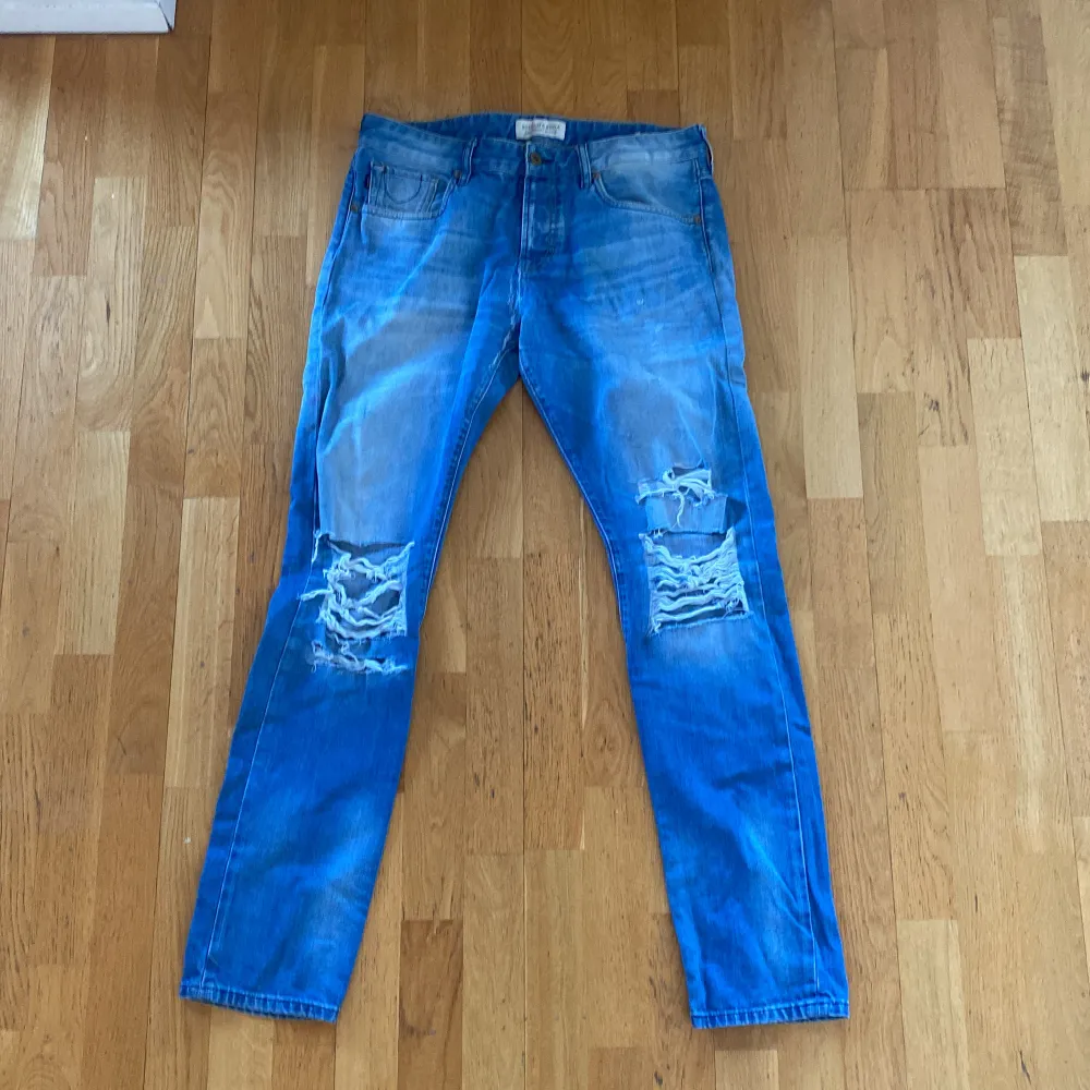 Slitna jeans från Scotch & Soda med slitningar runt knäna och regular fit av modellen Ralston. Storlek 33/34. . Jeans & Byxor.