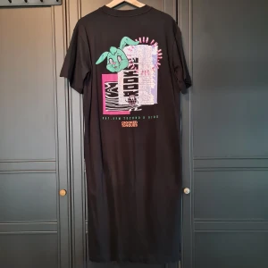 Svart t-shirt klänning med tryck  - Svart t-shirt klänning med tryck på ryggen. Sitter löst och är lite längre baktill. 