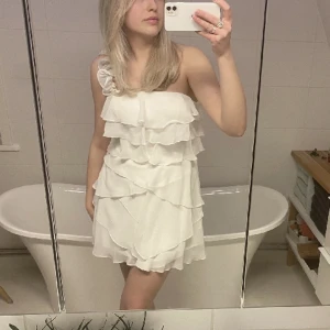 Vit volang klänning - Jättefin klänning till studenten. Har inbyggd bustier så man inte behöver ha bh under och har även ett till axelband om man inte vill ha den one shoulder. Aldrig använd och säljer då den var för stor för mig. Bilderna är lånade från hon jag köpte den av❤️