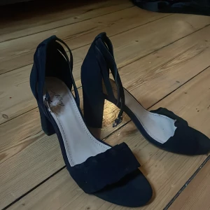 Svarta klackskor  - Svarta klackskor med lite frill! Har även band runt ankeln! Endast använda 1 gång! 