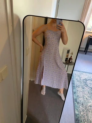 Syrénlila midiklänning  - Superskön luftig klänning med fint mönster, perfekt i sommar! 🌸🌸 Lätt att justera, har dragkedja i sidan, resår baktill samt snörning för att justera axelbanden! ☺️  Jag är ca 160cm lång för referens!