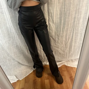 Skinnbyxor med slit - Jätte fina skinn/läder imiterade byxor med slit från Nelly i storlek XS. Dem är jätte höga i midjan och är långa på mig som är 168! jätte fint skick då dem bara är använda ett fåtal gånger 