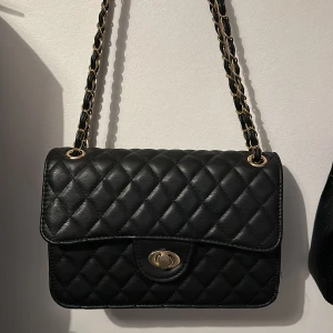 Axelväska - En superfin axelväska i svart och guld🌸 Det går att ändra längden på bandet så du kan ha den kort på axeln eller lång.