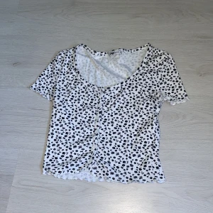 blommig tshirt med knappar - en vit t-shirt med svarta blommor, har knappar som man kan knäppa upp