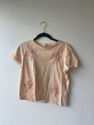 Aprikosfärgad t-shirt - T-shirt i fint skick med broderade blommor, storlek s