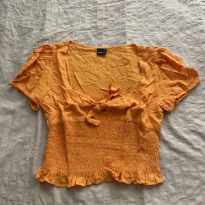 Orange topp - Orange topp köpt från Gina tricot, jätte fin färg. Fin urringning med en rosett vid brösten.