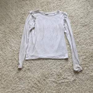 Vit volangtröja - Säljer denna fina långärmade volangtröjan då den är för liten. Den har andvändts ett par gånger men är forfarande i ett helt okej skick. Den är i storlek 158/164 men sitter som en S.