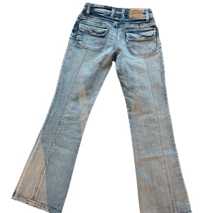 Jeans - Jeans med ljus tvätt men mörkare detaljer. Fickor med knapp där bak.  Söm längst med benen där bak. 