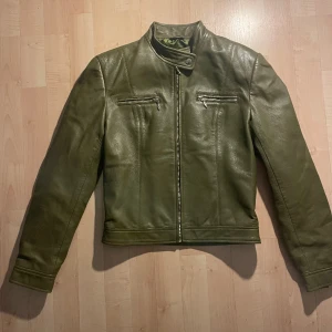 Olivgrön skinnjacka  - Olivgrön skinnjacka som är nästan helt oanvänd. Är osäker på om det är äkta skinn. Strorklen är 12 som jag tror motsvarar 34/36