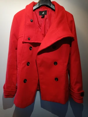 En röd kort kappa från H&M i storlek 40. Ny skick!  - Helt oanvänd kort kappa ifrån H&M i storlek 40! 