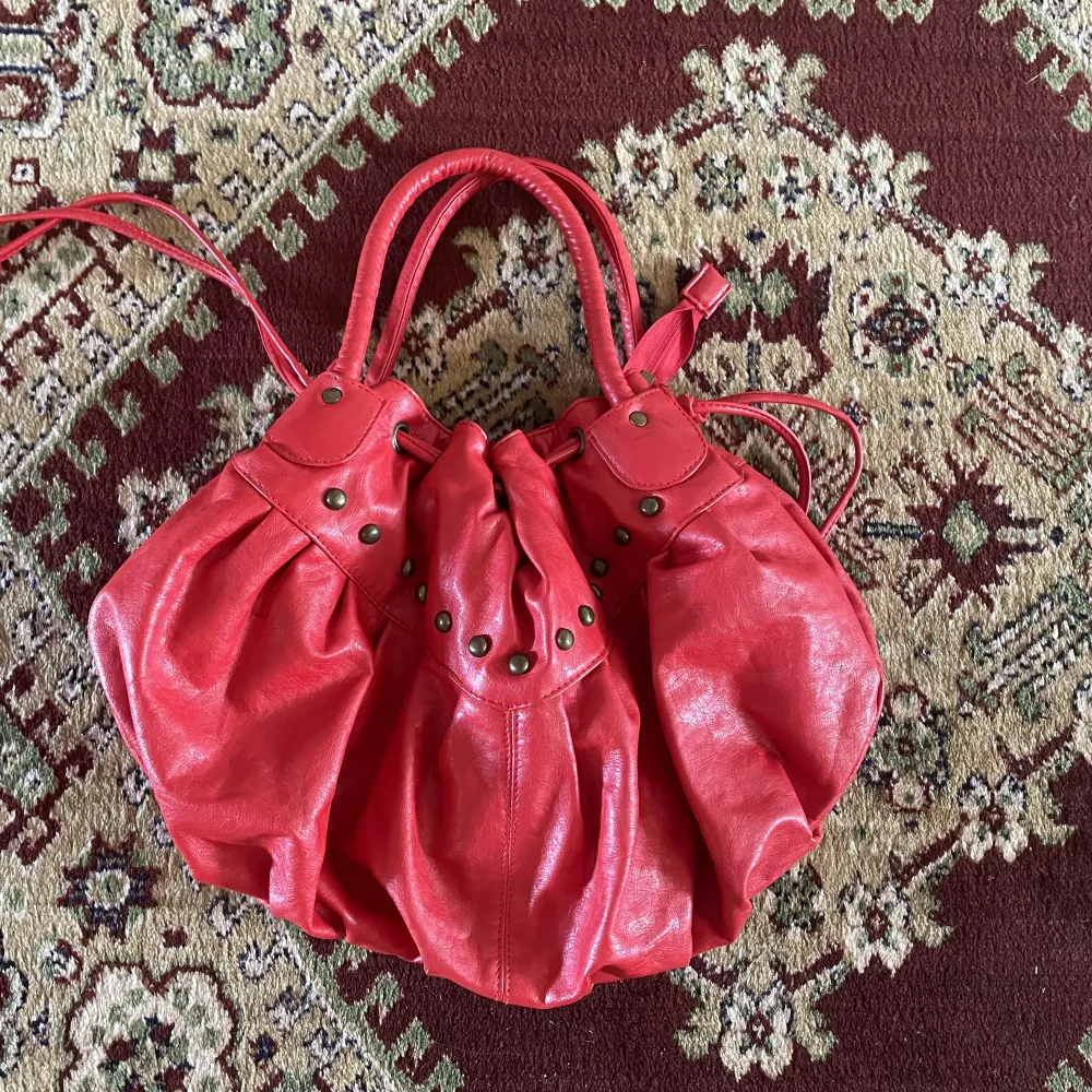 röd handväska med åtsnörning upptill för att variera väskan längd. coola nitar på framsidan, dragkedja för att stänga och två extra fack inuti. . Väskor.