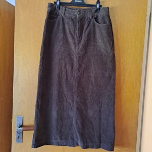 Brun kjol i manchester  - Str 38. Litet hål bak vid slit'en. Men kan fixas.  Midjan är ca 38 cm mätt rakt över, så blir ju 2x. Längd ca 85 cm. Modell är a-linjekjol. Pris är diskuterbart vid snabb affär. 💖 Vid funderingar skicka gärna pm. 😊