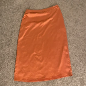 Korallfärgad kjol - Kjolen slutar strax nedanför knäna och är lite glansig i tyget. Har även en dragkedja på sidan.