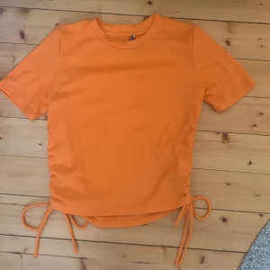 Tajt t-shirt med snören  - Säljer denna orangea tröjan då den inte kommer till någon användning, den är bara använd Max 1-2 gånger. Fint skick bara att lappen bak i nacken är lös men inget som påverkat tröjans utseende! Nypris: Kanske 100kr