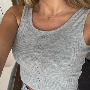 Croptop mer knappar i fram - Grå Crop top med Fake-knappar i fram som detalj. Ribbat material. Storlek S