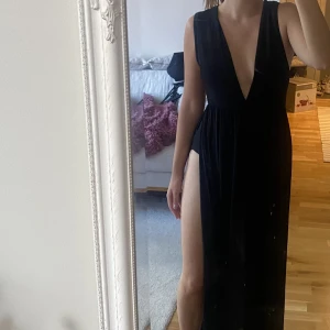 Svart långklänning - Festlig långklänning med body och  slits från midjan på båda sidorna! Djup urringning. Endast använd en gång, mycket fint skick! Jag är 165 cm lång och slutar strax över fötterna!